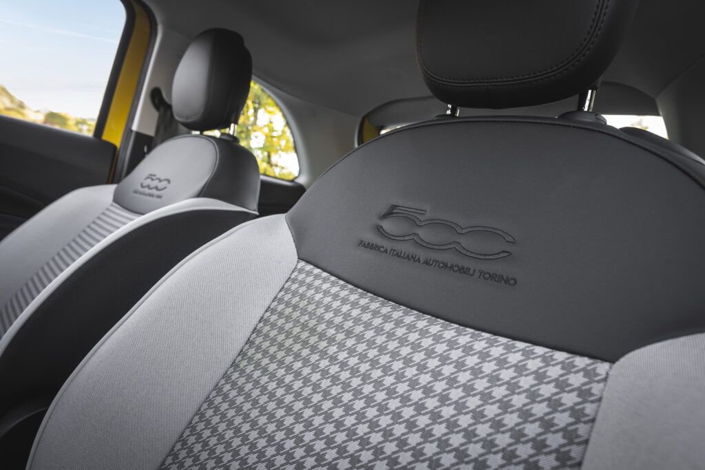 Detailaufnahme der Vordersitze des Fiat 500 Hybrid mit gesticktem 500-Logo und zweifarbigem Stoffbezug.