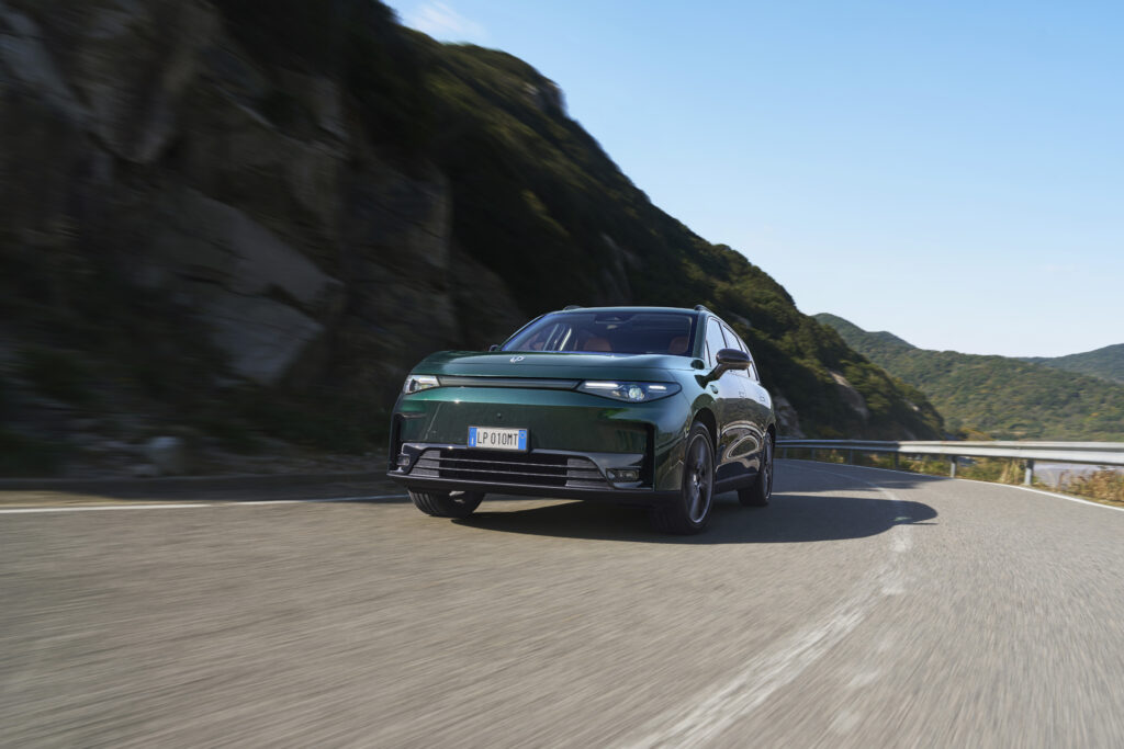 Dunkelgrüner Leapmotor C10 fährt auf einer kurvigen Straße durch eine bergige, grüne Landschaft.