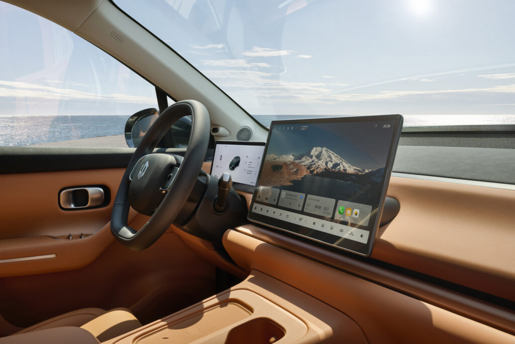 Heller Innenraum des Leapmotor C10 mit orangefarbenem Armaturenbrett, Lenkrad und zwei digitalen Displays vor dem Meer.