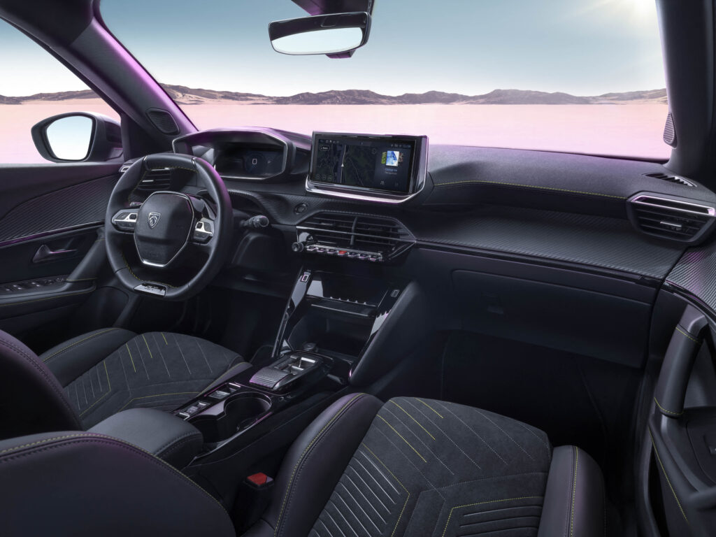 Blick auf den dunklen Innenraum mit Lenkrad, digitalem Cockpit, zentralem Touchscreen, Mittelkonsole und Vordersitzen mit grünen Ziernähten.