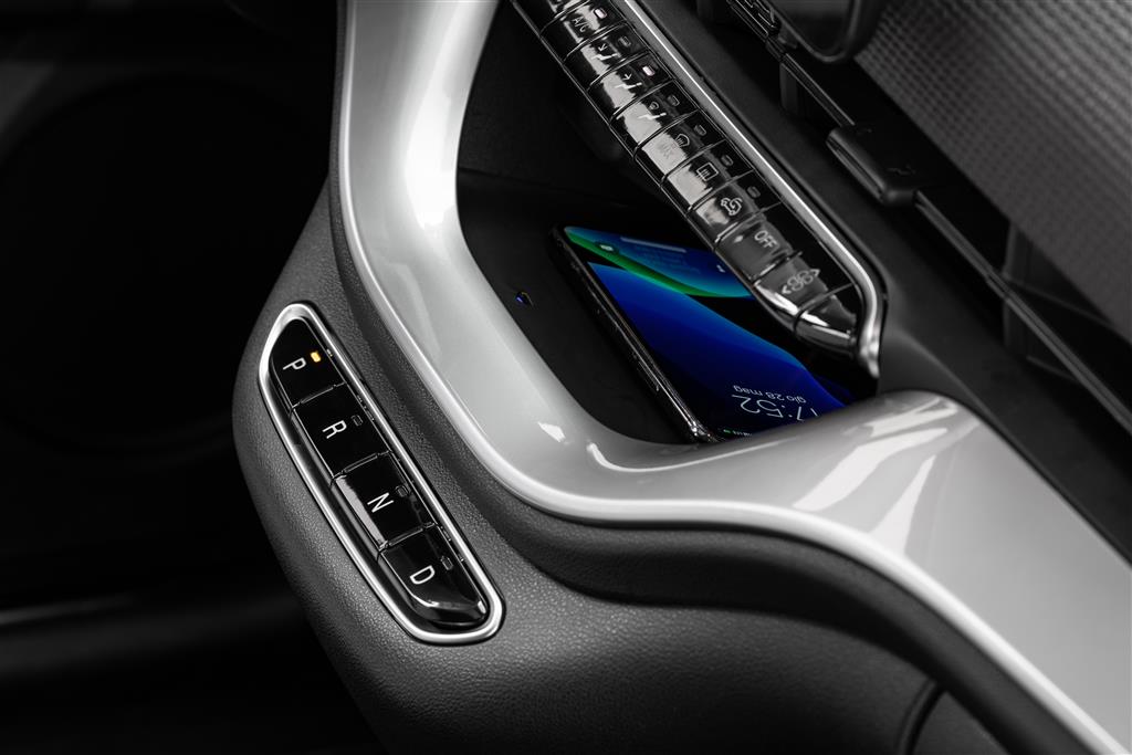 Detailaufnahme der Mittelkonsole im Fiat 500 Elektro. Links befinden sich die Gangwahltasten P, R, N und D. In der von einer hellen Verkleidung eingefassten Ablage liegt ein Smartphone unterhalb einer Reihe glänzender Bedientasten.