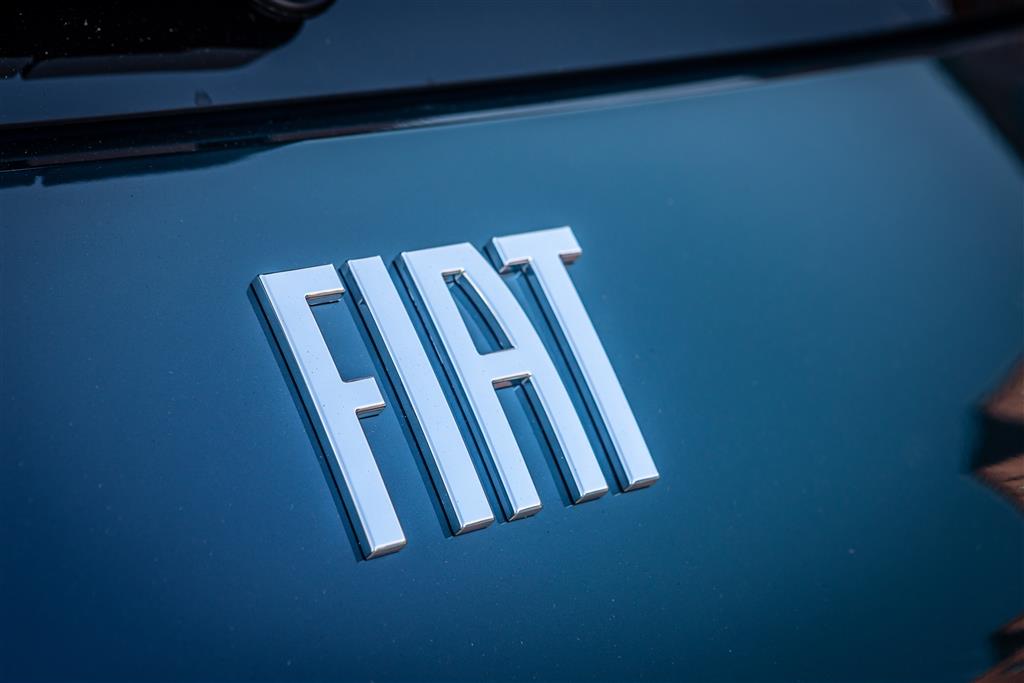 Nahaufnahme des silberfarbenen Fiat-Schriftzugs auf der dunkelblauen Karosserie eines Fiat 500 Elektro. Die erhabenen, metallisch glänzenden Buchstaben heben sich deutlich von der glatten, lackierten Fahrzeugoberfläche ab.