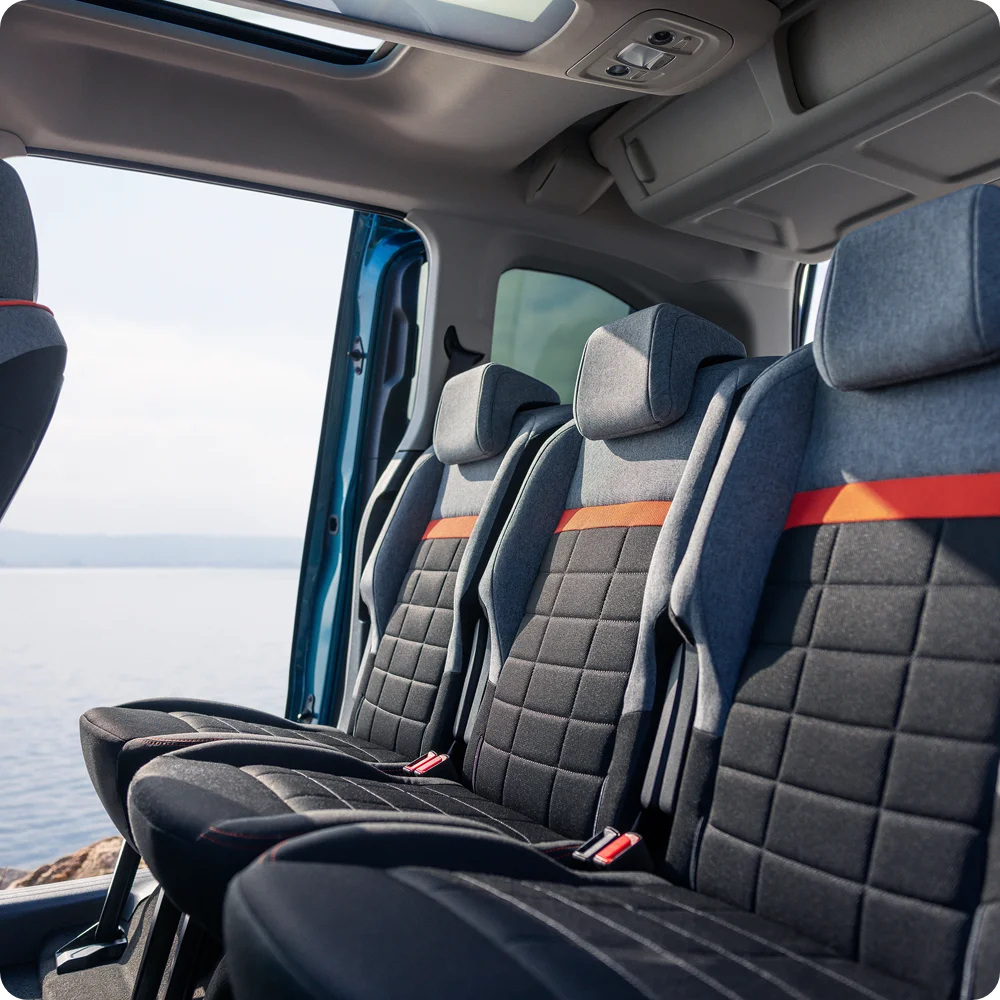 Blick in den Innenraum des Citroën Berlingo mit drei separaten Sitzen in der zweiten Sitzreihe. Die dunklen Stoffsitze verfügen über Kopfstützen und Sicherheitsgurte. Durch die großen Seitenfenster fällt Tageslicht in den Fahrgastraum.